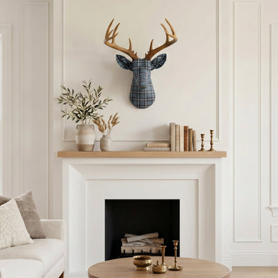 Plaid fabric deer head wall decor with gold antlers mounted above a neutral farmhouse fireplace mantel with books and greenery